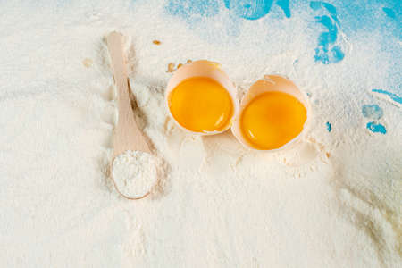 cracked egg with flour and spoon on blue backgroundの写真素材