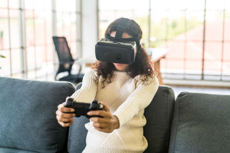 Latin woman using a virtual reality headset on sofaの写真素材