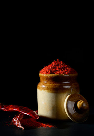Red Chili Pepper powder in clay pot with Red Chili Peppers on black background