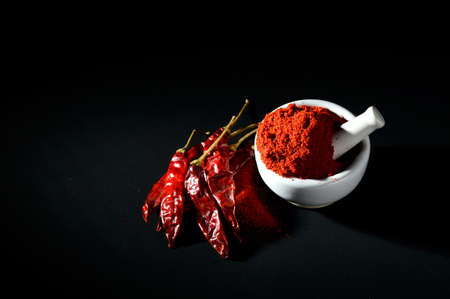 Red Chili Pepper powder in pestle with mortar and Red Chili Peppers on black backgroundの写真素材
