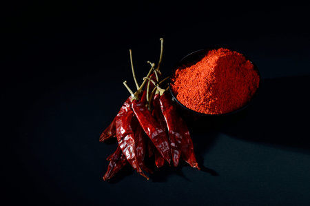 chilly powder in black bowl with red chilly, dried chillies on black background