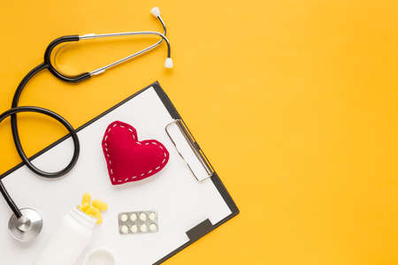stethoscope stitched heart medicine falling from bottles blister packed medicine with clipboard yellow table. High quality beautiful photo conceptの写真素材