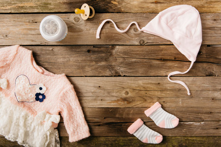 pink baby s dress with headwear pair socks milk bottle pacifier wooden tableの写真素材
