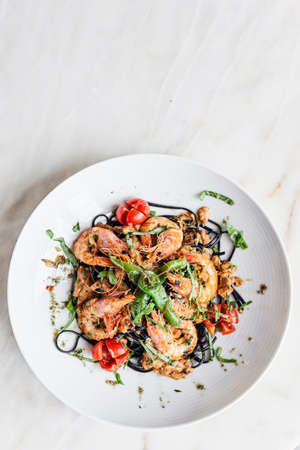 gourmet grilled prawn and vegetables on black squid ink pastaの写真素材
