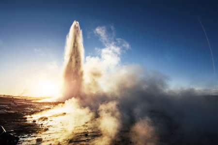 Eruption of Strokkur geyser in Iceland. Winter cold colors, sun lighting through the steamの写真素材