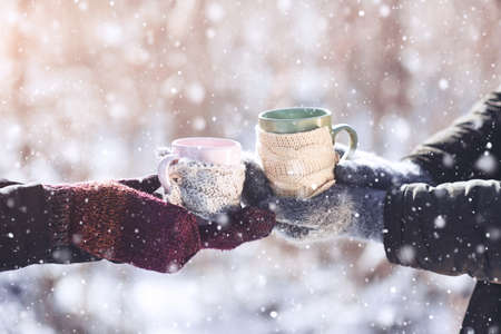 Couple hands in mittens take a mugs with hot tea in winter parkの写真素材