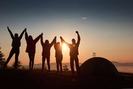 A silhouette of group people have fun at the top of the mountain near the tent during the sunsetの写真素材