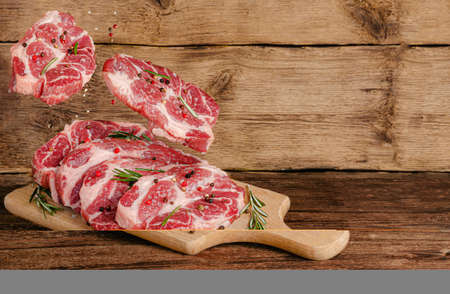 Flying pork steaks over board with meat and spices on wooden background. Copy spaceの写真素材
