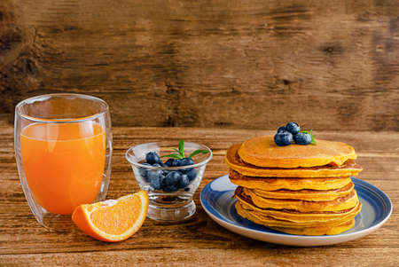 Heap of pumpkin pancakes with blueberries and orange juice on rustic wooden background. Copy space.の写真素材