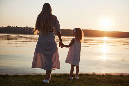 Mom plays with her baby on holidays near the ocean, silhouettes at sunsetの写真素材