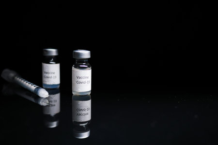 Close up of coronavirus vaccine and syringe on black background.