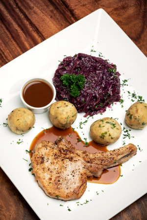 german style grilled pork chop with bread dumplings and red cabbage traditional meal on wood tableの写真素材