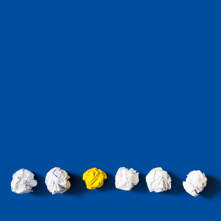 yellow crumpled paper ball among white balls against blue backgroundの写真素材