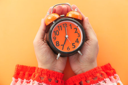 women hand holding alarm clock orange background