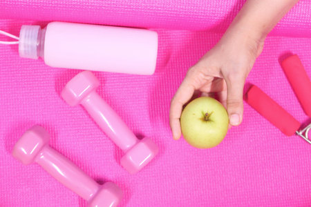 apple , pink color dumbbell, water bottle on exercise mat .