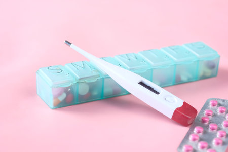 digital thermometer, pill container on a pink background .