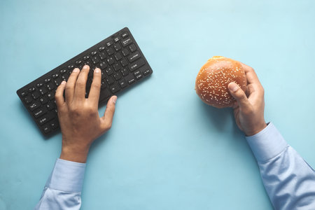 young man typing on keyboard while holding a burger ,の写真素材