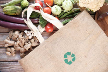 reusable shopping bag with recycled arrows sign and vegetables on table ,の写真素材