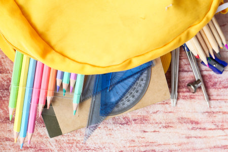 Top view of yellow backpack with different colorful stationery on table