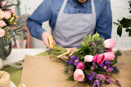 close up male florist cutting paper wrapping flower bouquet