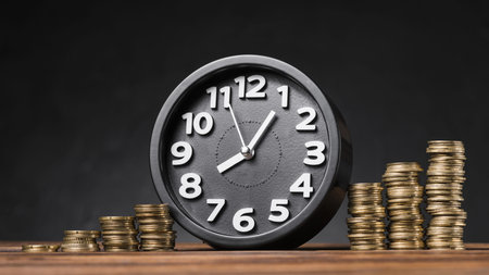 round clock between the increasing coins on wooden desk against black backdrop . Resolution and high...