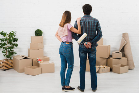rear view young couple looking white painted wall with cardboard boxes