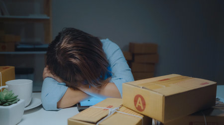 Young Asian entrepreneur business woman owner of SME sleepy exhausted working at office desk in...