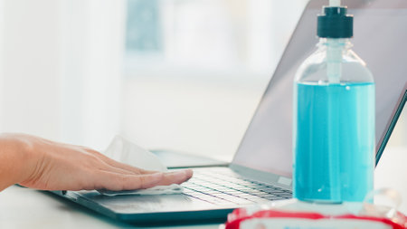 Asian woman using alcohol spray on tissue clean laptop before open for protect coronavirus. Female clean computer for hygiene when social distancing stay at home and self quarantine time.の写真素材