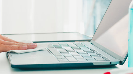 Asian woman using alcohol spray on tissue clean laptop before open for protect coronavirus. Female...