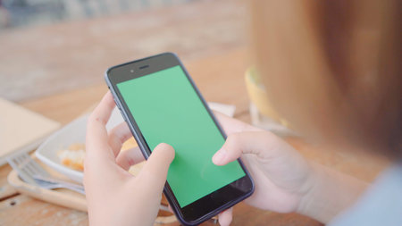 Young asian woman using black mobile phone device with green screen. Asian woman holding smartphone,...