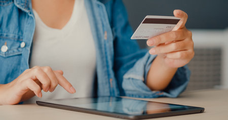 Young asia lady using tablet order online shopping product and paying bills with credit card in living room interior. Stay at house, Self quarantine activity, Fun activity for coronavirus prevention.の写真素材