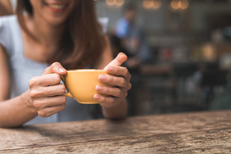 Cheerful asian young woman drinking warm coffee or tea enjoying it while sitting in cafe. Attractive happy asian woman holding a cup of coffee.の写真素材