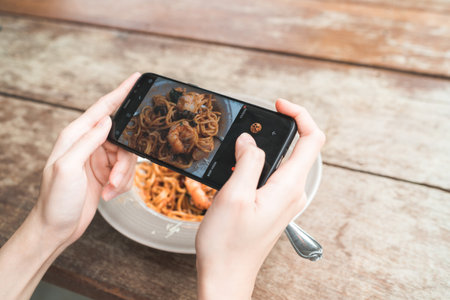 Female blogger photographing lunch in restaurant with her phone. A young woman taking photo of spaghetti food on smartphone, photographing meal with mobile camera.の写真素材