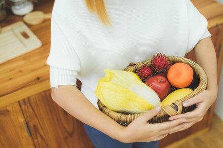 Asian beautiful woman holding fruit and vegetable in the kitchen at her home. Happy pretty asian female eat freshness fruit for healthy body. lifestyle asia woman at home concept.の写真素材