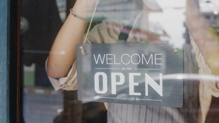 Young Asia girl wear face mask turning a sign from closed to open sign on door looking outside...