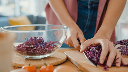 Hand of young Asian woman chef hold knife cutting Red Chinese cabbage on wooden board on kitchen table in house. Cooking vegetable salad, Lifestyle healthy food eating and traditional natural concept.の写真素材