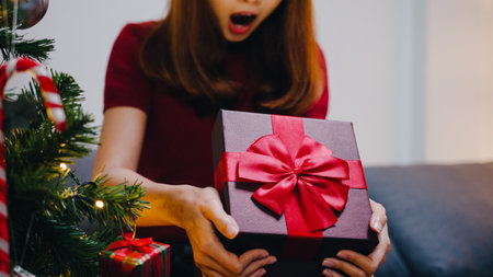 Young Asia female having fun opening X'Mas present box near Christmas tree decorated with ornaments in living room at home. Merry Christmas night and Happy New Year holiday festival.の写真素材