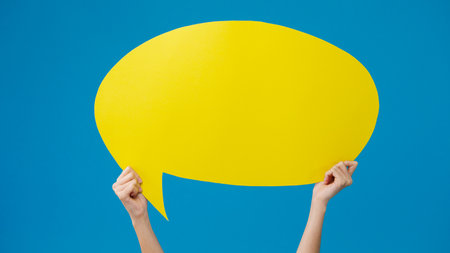 Young teen girl holding with copyspace cartoon speech bubble in hand over blue background. Copy space for place a text, message for advertisement. Advertising area, mockup promotional content.の写真素材