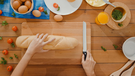 Hands of young Asian woman chef hold knife cut whole grain bread on wooden board on kitchen table in...