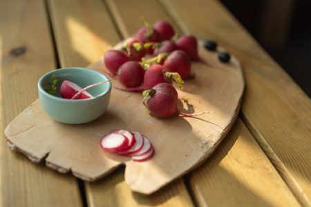 The afternoon sun shines on the wooden plate, complete and sliced red radishの写真素材