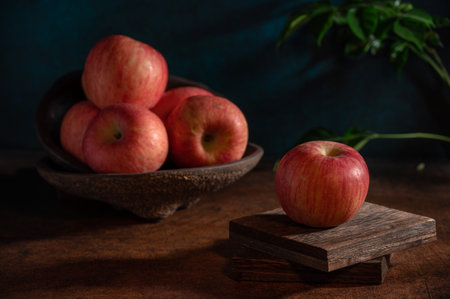The apples on the plate look like oil paintings under the dim light on the wood grain tableの写真素材