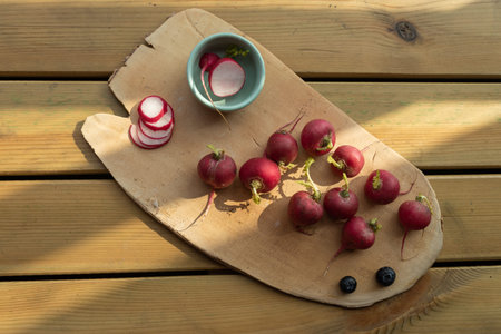 The afternoon sun shines on the wooden plate, complete and sliced red radishの写真素材