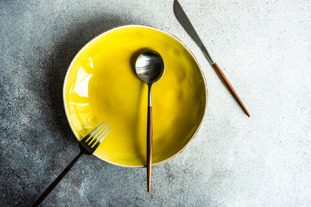 Minimalistic place setting with ceramic plate and modern cutlery set on concrete backgroundの写真素材