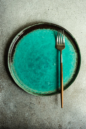 Minimalistic place setting with ceramic plate and modern cutlery set on concrete backgroundの写真素材