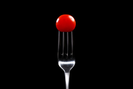Fork with cherry tomato close-up. Isolated image on a black background. Macro photo. cooking concept.の写真素材