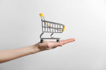 closeup of a woman's hand holding a small metal empty shopping cart in the palm of her hand on gray background. The concept of shopping. copy space for advertisingの写真素材