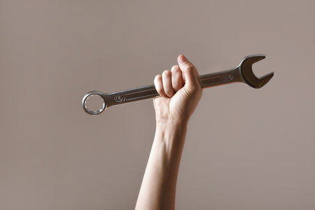 big spanner in the woman's hand. hand holds a wrench on a gray background. Combination wrench. big chrome vanadium spanner in the hand. women's work. labor dayの写真素材
