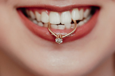 Close up young bride showing her wedding ring holding in teeth and smiling. woman with diamond ring...