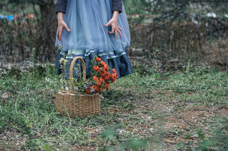 A yellow basket on the grass contains red flowersの写真素材