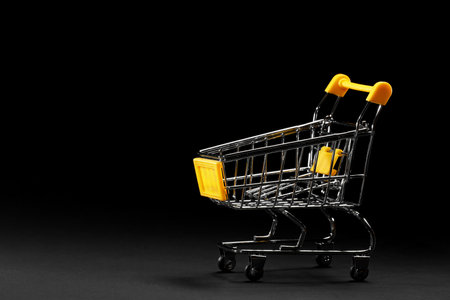 Close up of supermarket grocery push cart for shopping with yellow plastic elements on handle isolated on black background. Concept of shopping. Copy space for advertisementの写真素材